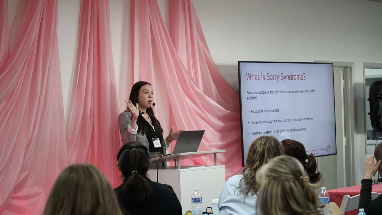 A speaker at a previous WoF conference in front of a screen that says, 'What is Sorry Syndrome?'