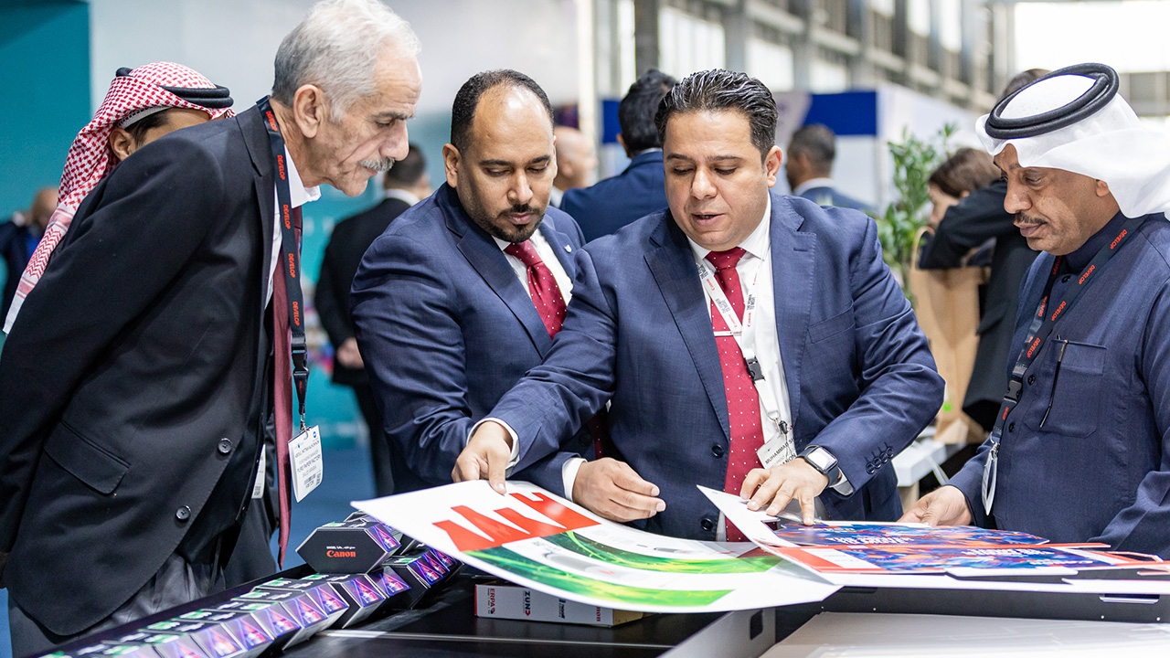 Four men look at a printed product sample