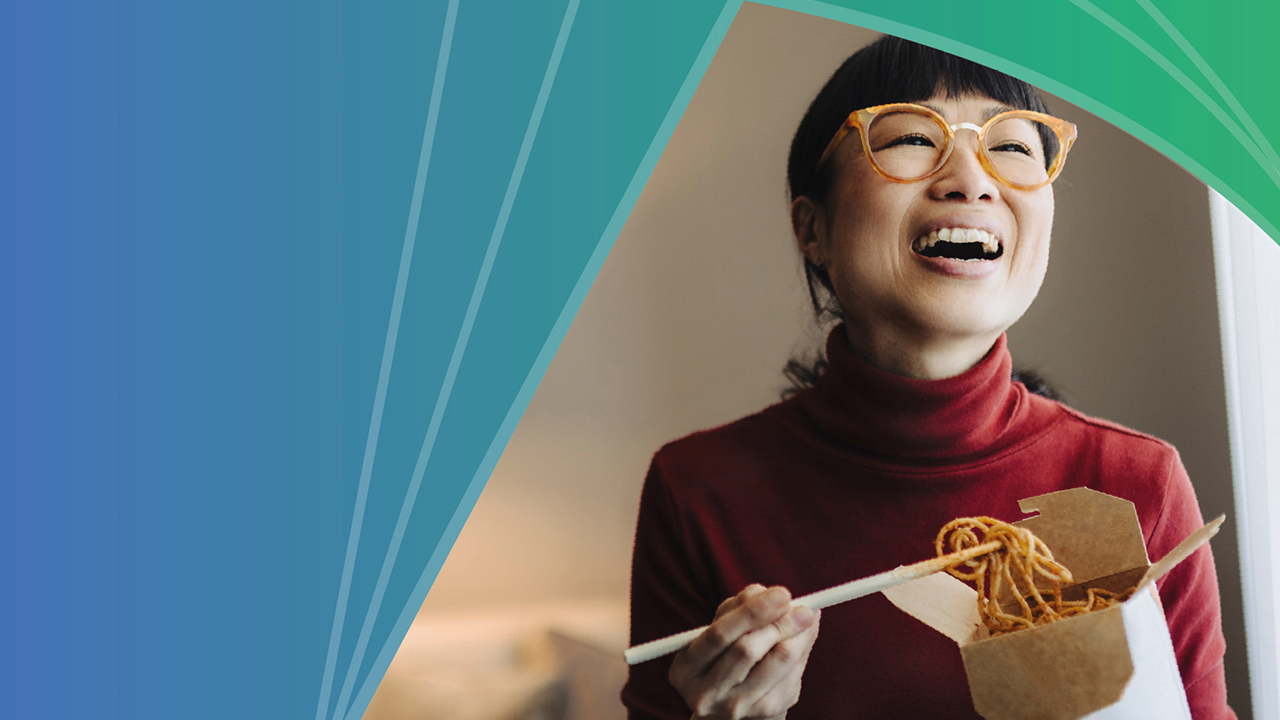 A woman eats noodles out of a cardboard takeout container