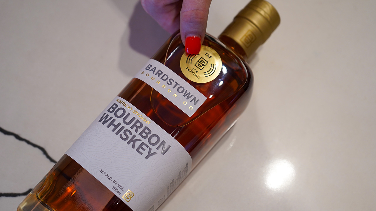 A hand applies a label that says 'Tap - It's personal' to a bottle of bourbon