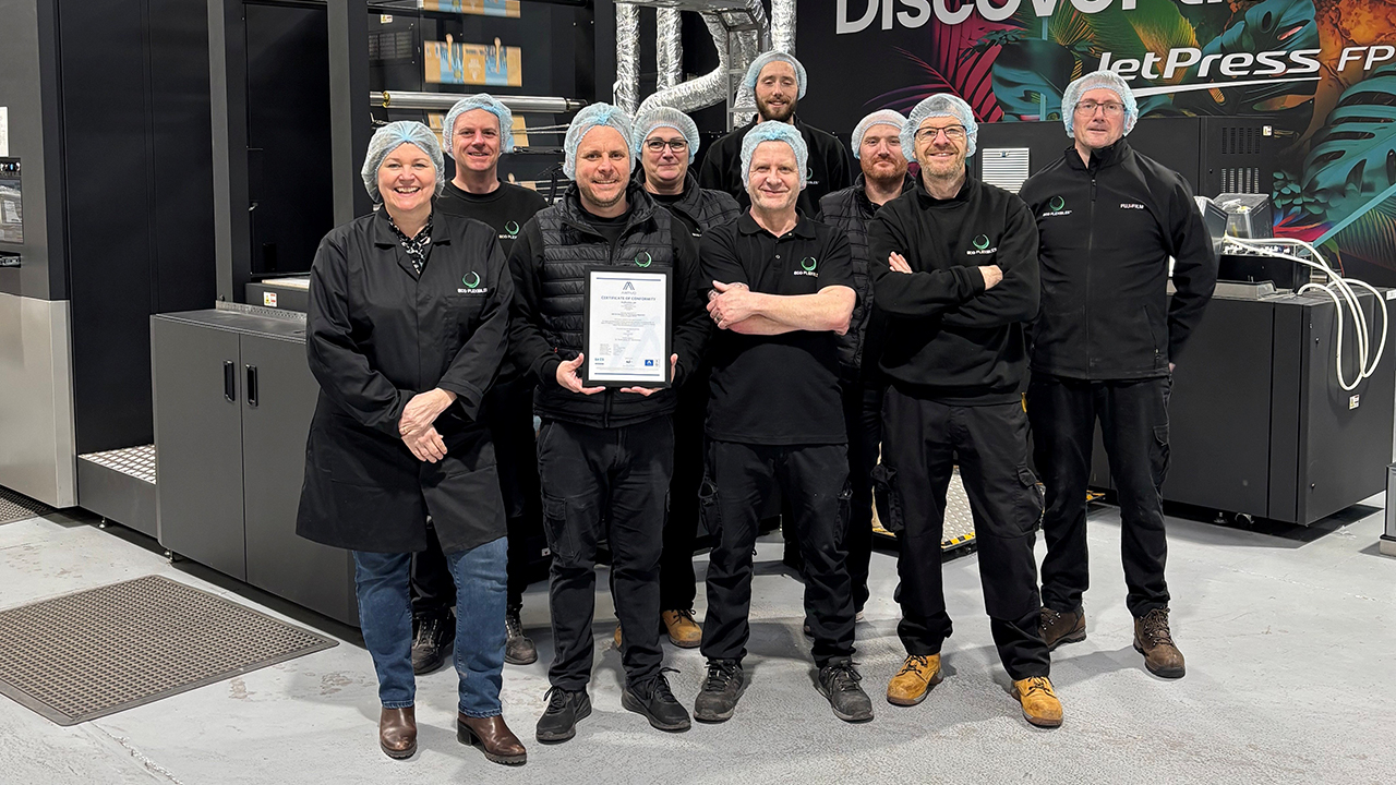A group of employees stand in a facility, with one in the middle holding the certification