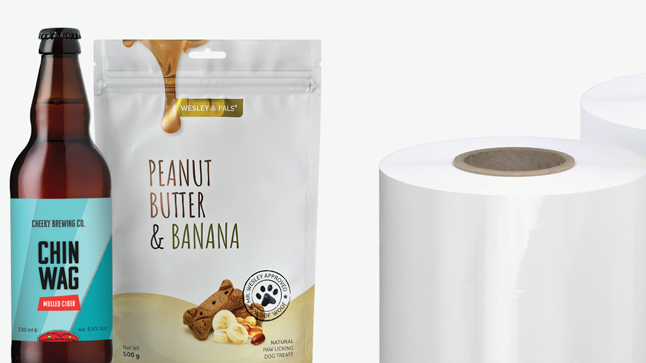 A roll of the new film next to a beer bottle and flexible package featuring labels made of the film