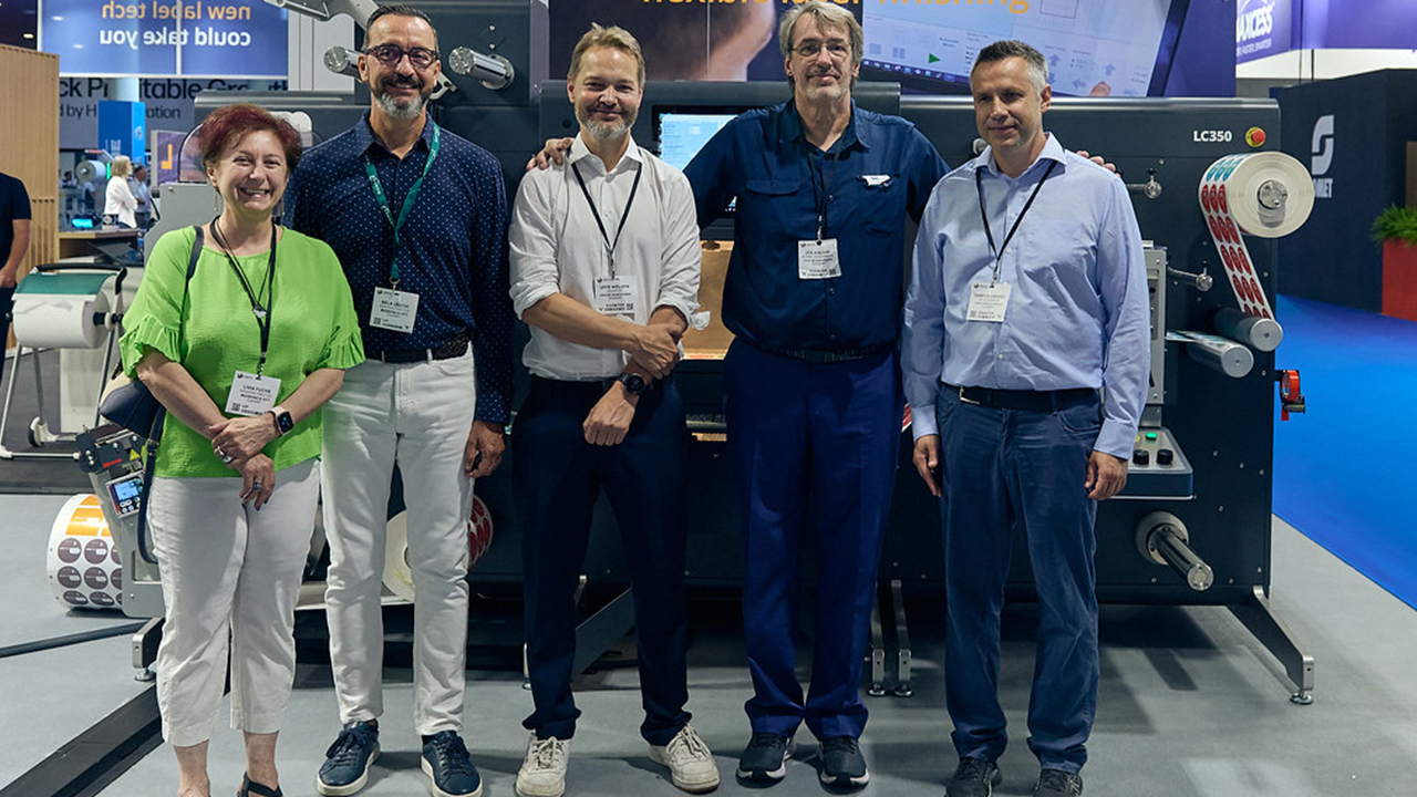 A group of employees stand in front of the die-cutter at Labelexpo